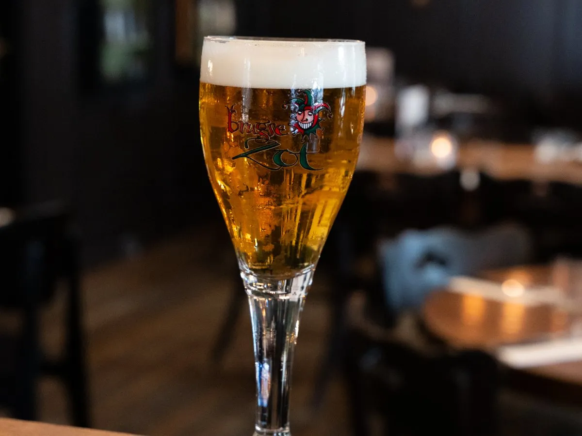 Een glas Brugse Zot met schuimkraag op een houten reling