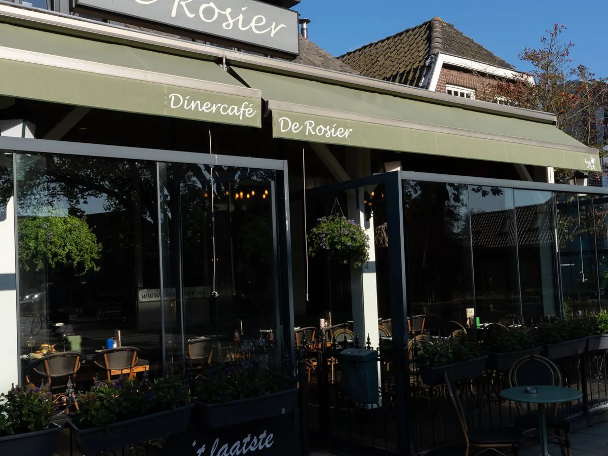De gevel van De Rosier met de luifels, het terras en het krijtbord op de stoep