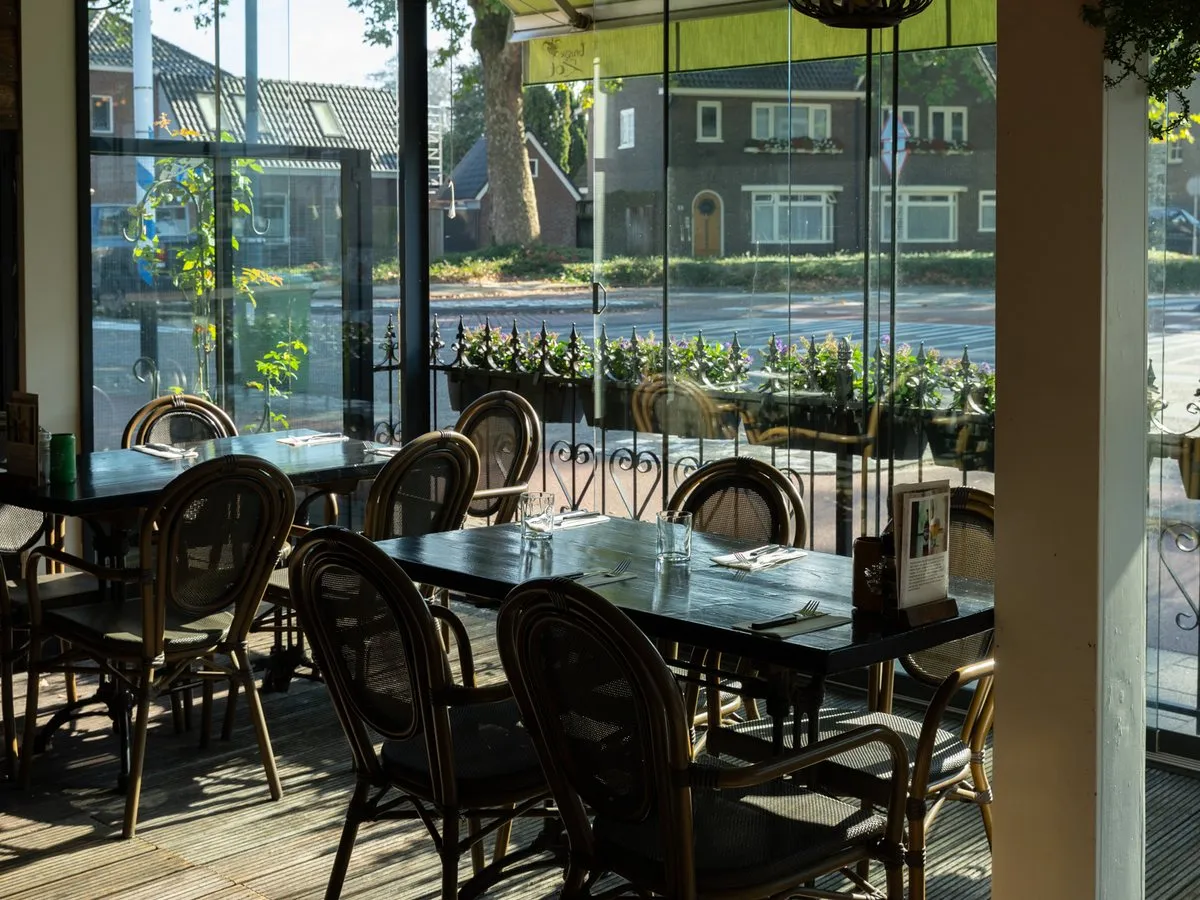 Het overdekte terras met rieten stoelen en een glazen wand naar de straat