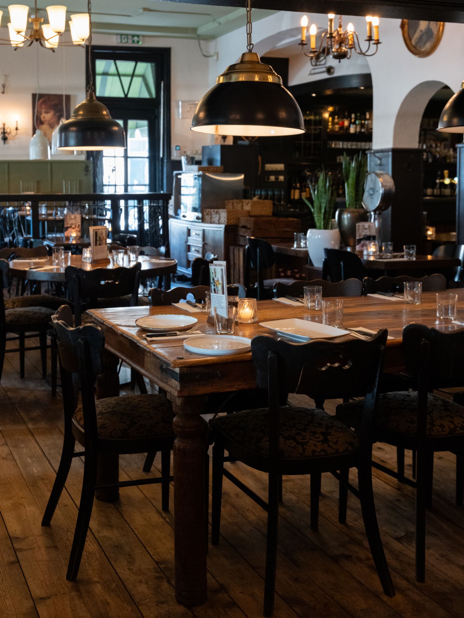 Een lange houten tafel met kaarsjes onder de hanglampen in de zaal van De Rosier