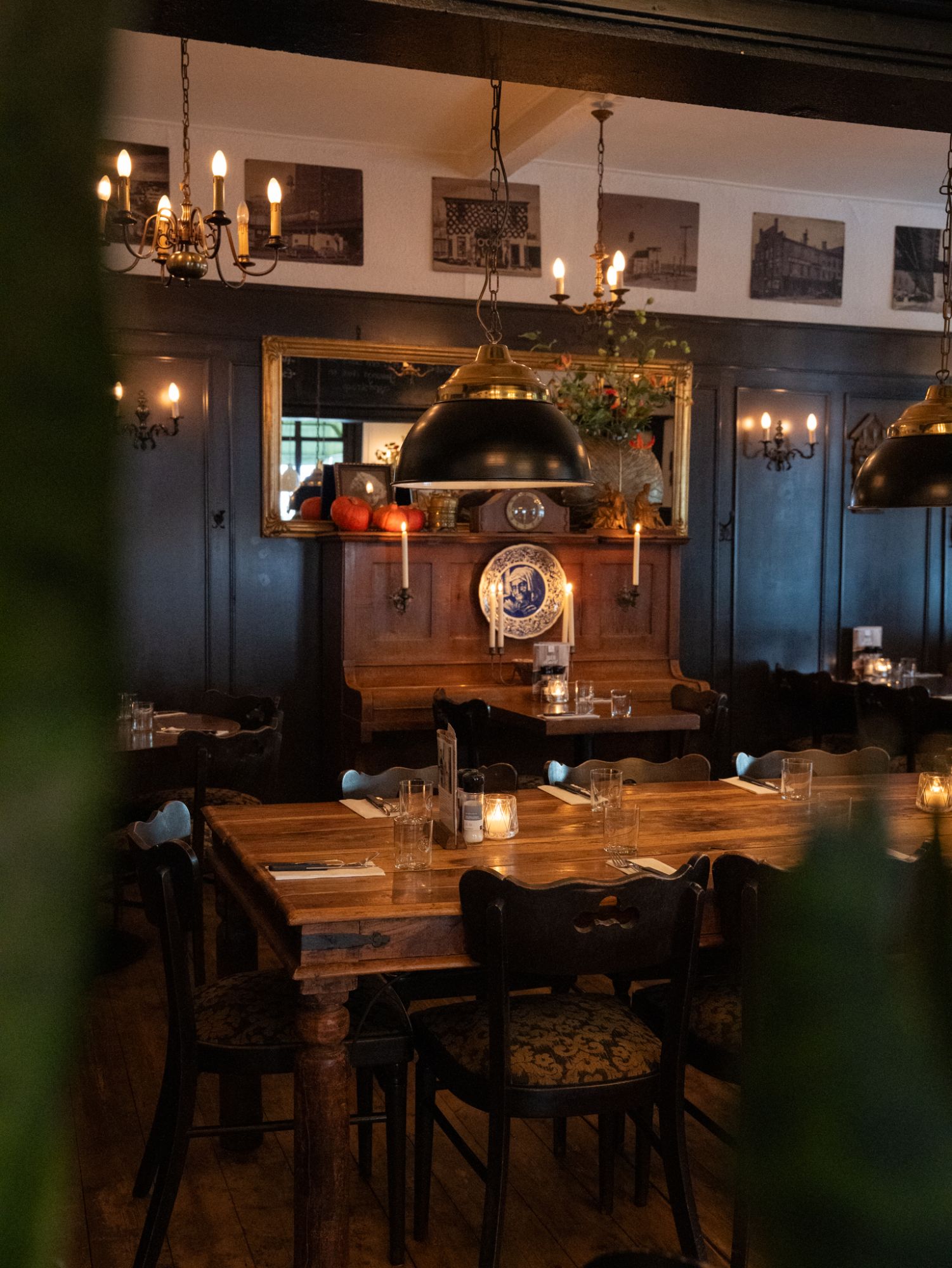 De zaal van De Rosier met een gedekte houten tafel, een oude piano met een Delfts blauw bord en kaarsen onder een zwarte hanglamp